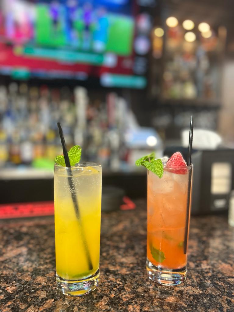 Two colorful specialty cocktails garnished with mint and fruit